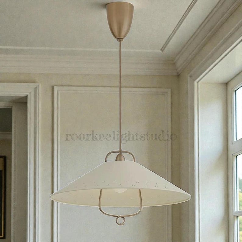 May include: Cream-coloured pendant light with a wide, conical shade and a metal frame. The light fixture is suspended from the ceiling by a thin rod and a decorative canopy. The text "roorkeelightstudio" is visible on the shade.