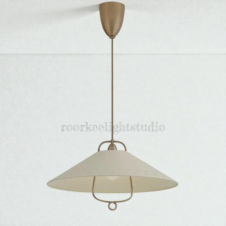 May include: A cream-coloured pendant light with a conical shade and a bronze-coloured metal frame. The light hangs from a matching bronze-coloured ceiling mount. The shade has small, decorative perforations. The text "roorkeelightstudio" is visible.