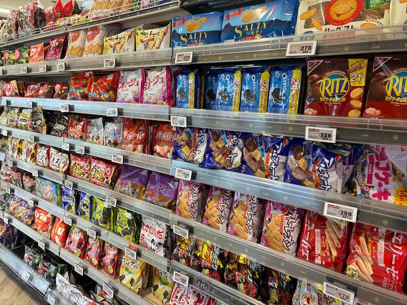 Peut inclure: &Eacute;tag&egrave;res de supermarch&eacute; remplies de collations emball&eacute;es, notamment des biscuits, des crackers et des gaufrettes. Des marques comme Ritz, Oreo et Salty sont visibles. Une grande vari&eacute;t&eacute; de produits est pr&eacute;sent&eacute;e.