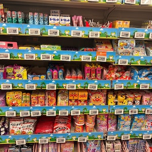 Peut inclure: &Eacute;tag&egrave;re de supermarch&eacute; remplie de diverses collations et bonbons japonais. Les &eacute;tag&egrave;res sont d&eacute;cor&eacute;es d'un motif tropical bleu et vert. Les produits comprennent des bonbons emball&eacute;s, des gommes et d'autres friandises.