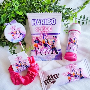 Op de afbeelding: Een feestset bestaande uit een zakje Haribo-snoep, een M&M's-reep, een roze bellenblaas en een felroze scrunchie, gepersonaliseerd met de naam Chloé, de tekst 9 ans en een afbeelding van drie personages in een roze ster.