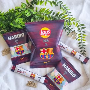 Op de afbeelding: Een assortiment snacks, waaronder Lay's chips en Haribo snoep, met een FC Barcelona thema. De verpakking toont het logo van het team en het nummer 19. Kinder Maxi chocoladerepen en een gouden "Happy Birthday" decoratie zijn ook aanwezig.