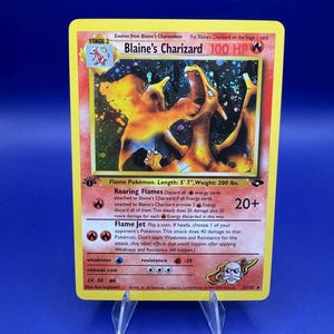 Könnte beinhalten: Eine gelbe Blaine's Charizard Pokémon-Karte. Die Karte zeigt eine feurige orangefarbene Charizard-Illustration mit dem Text "Blaine's Charizard 100 HP". Die Karte ist 170 cm lang und wiegt 90 kg.