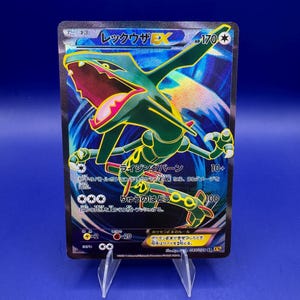 May include: A holographic Pokémon trading card featuring Rayquaza EX. The card has a green and yellow dragon illustration with Japanese text. The card is displayed on a clear plastic stand against a blue background.