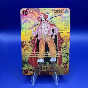 May include: A trading card featuring a character with a red coat, pink shirt, and orange pants, holding a sword. The card has a gold background with the number "10" and the text "13000". The card is displayed on a clear stand against a blue backdrop.