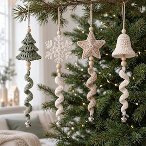 May include: Four hanging ornaments featuring crocheted shapes: a sage green tree, a white snowflake, a beige star, and a cream bell. Each ornament includes wooden beads, a long crocheted spiral tail, and a small silver bell at the bottom.
