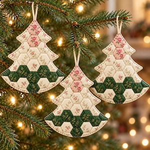 Puede incluir: Tres adornos navideños acolchados con un diseño de patchwork hexagonal. La tela muestra un patrón de pequeñas rosas rosadas sobre fondos crema y hexágonos de color verde oscuro con delicadas ramas botánicas doradas.