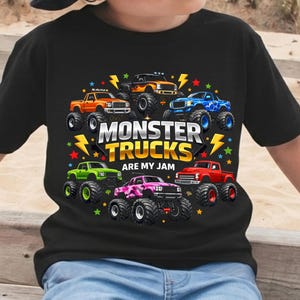 May include: Black t-shirt featuring a colorful graphic of monster trucks. The design includes seven trucks in various colors, surrounded by stars and lightning bolts, with the text "MONSTER TRUCKS ARE MY JAM".