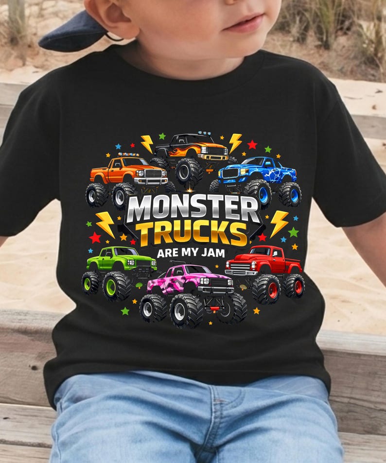 May include: Black t-shirt featuring a colorful graphic of monster trucks. The design includes seven trucks in various colors, surrounded by stars and lightning bolts, with the text "MONSTER TRUCKS ARE MY JAM".