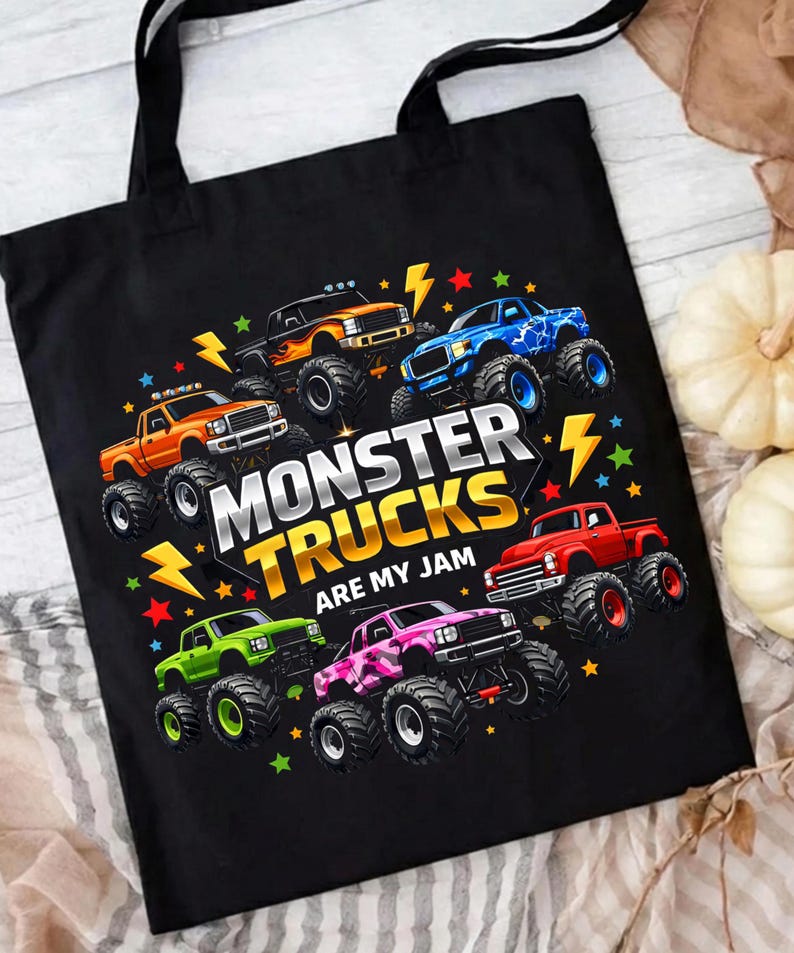 May include: Black tote bag featuring a colorful graphic of monster trucks. The design includes various trucks in orange, blue, green, pink, and red, with the text "MONSTER TRUCKS ARE MY JAM" and lightning bolt accents.