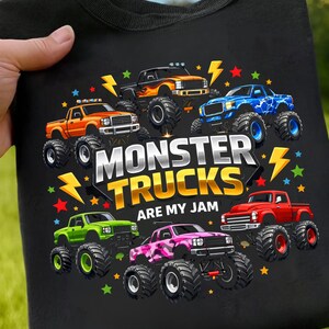 May include: Black t-shirt featuring a colorful graphic of seven monster trucks in various colors, including orange, blue, and green. The text "MONSTER TRUCKS ARE MY JAM" is prominently displayed.