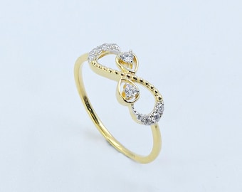 Könnte beinhalten: Ein goldfarbener Ring mit einem Unendlichkeitszeichen-Design. Das Unendlichkeitszeichen ist mit kleinen, klaren Edelsteinen verziert. Der Ring hat ein zartes Band und eine polierte Oberfläche, geeignet für den Alltag oder besondere Anlässe.