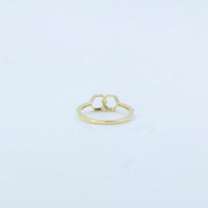 May include: A gold ring featuring a double hexagon design. The ring is adorned with small, sparkling stones along the band and within the geometric shapes. The ring is set against a white background.
