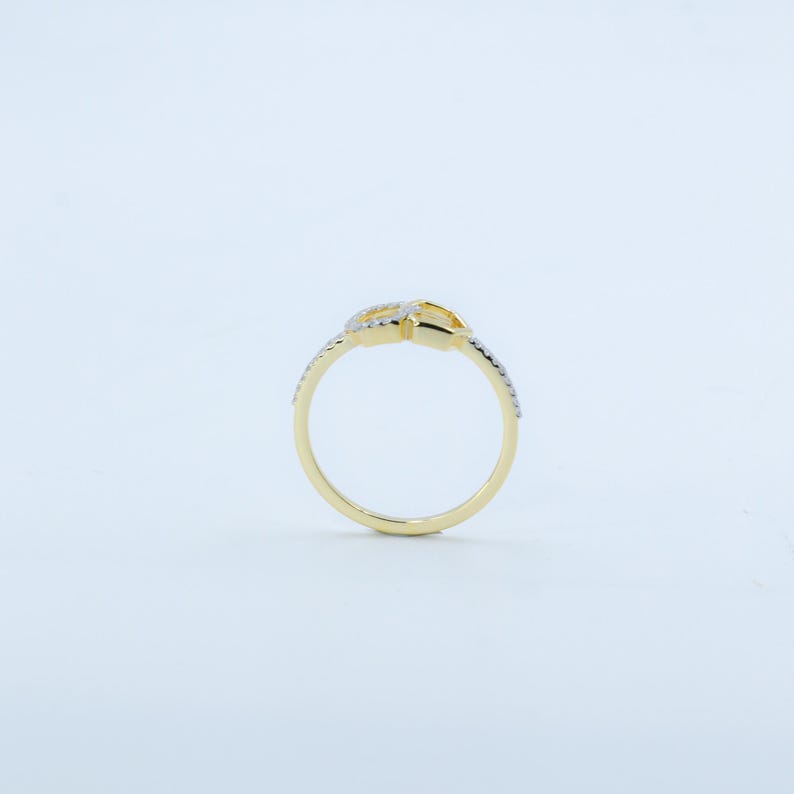 May include: A gold-colored ring with a knot design. The ring features small, clear gemstones along the band and on the knot. The ring is set against a white background, highlighting its details.