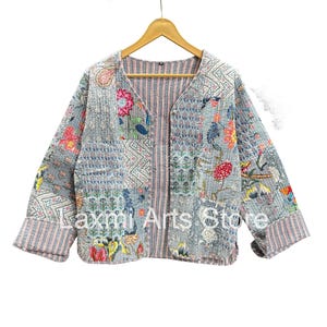 Puede incluir: Chaqueta patchwork con cuello en V y mangas largas. La chaqueta presenta una variedad de estampados florales y geométricos en tonos azules, rosas y verdes. El texto "Laxmi Arts Store" es visible en la parte delantera de la chaqueta.