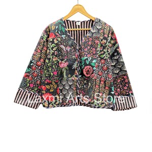 以下が含まれることがあります： 赤、ピンク、緑、白の花柄の黒いキルティングジャケット。 ジャケットはVネックで、ストライプのボーダーが付いています。 ジャケットの下部には「laxmi Arts Store」の文字が見えます。
