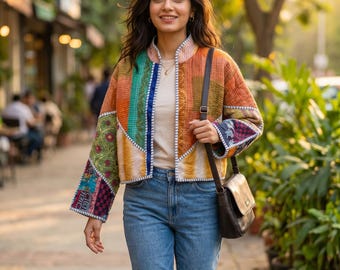 May include: A quilted jacket featuring a patchwork design of orange, green, yellow, and blue fabric panels with visible stitching. The jacket is worn over a plain beige shirt and blue denim jeans, paired with a dark brown leather shoulder bag.