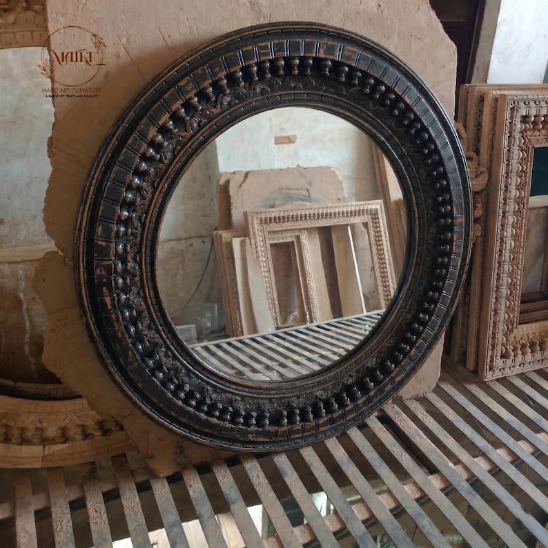 Pu&ograve; includere: Uno specchio rotondo marrone scuro con una cornice ornata e strutturata. La cornice presenta un motivo ripetuto di piccoli dettagli in rilievo. Lo specchio &egrave; esposto su una superficie di legno, con altre cornici di legno visibili sullo sfondo. Il diametro &egrave; di circa 60 cm.