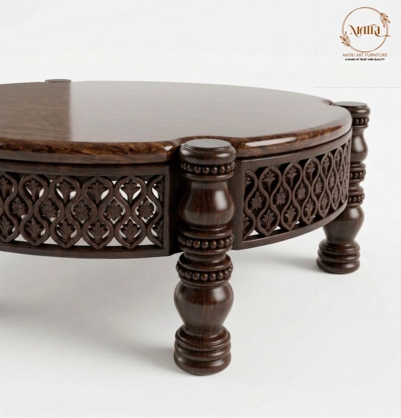 May include: A dark brown, round wooden coffee table with intricate carved detailing. The table features a decorative, openwork design around the sides and is supported by four sturdy, turned legs. The tabletop has a smooth, polished finish.