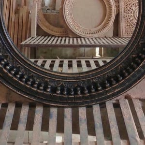 Pu&ograve; includere: Una cornice rotonda nera e ornata, con un design dettagliato e strutturato. La cornice &egrave; in legno e ha una finitura scura. Altre cornici in legno intagliato sono visibili sullo sfondo.