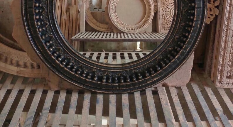 Pu&ograve; includere: Una cornice rotonda nera e ornata, con un design dettagliato e strutturato. La cornice &egrave; in legno e ha una finitura scura. Altre cornici in legno intagliato sono visibili sullo sfondo.