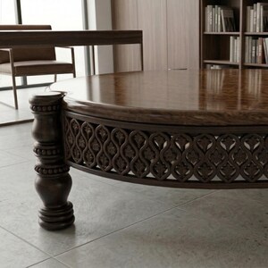 May include: A large, round, dark brown wooden coffee table with a glossy finish. The table features intricate carved detailing around the base and a decorative, turned leg. The table is in a room with a desk, chair, and bookshelves.