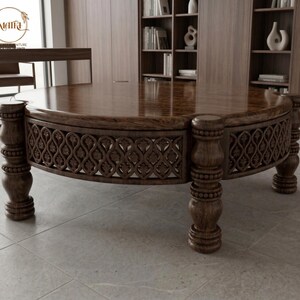 May include: A large, round wooden coffee table with a dark brown finish. The table features ornate carved detailing around the perimeter and is supported by four sturdy, turned legs. The tabletop has a polished, reflective surface.
