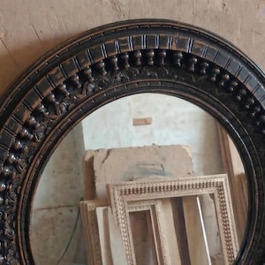 Pu&ograve; includere: Uno specchio ovale con cornice marrone scuro e dettagli ornati. La cornice presenta un design intagliato e strutturato. Lo specchio &egrave; esposto con altre cornici in legno, suggerendo un tema di arredamento o decorazione per la casa.