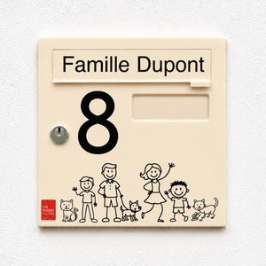 May include: A square, cream-colored mailbox featuring the text "Famille Dupont" and the number "8" in black. Below, a black line drawing depicts two adults, two children, a dog, and two cats. A small red square logo reads "ma maison mon style".