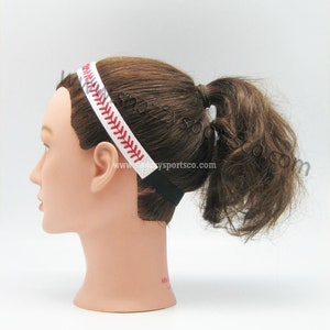 May include: White headband with red stitching, resembling a baseball. The headband is worn on a mannequin with brown hair.