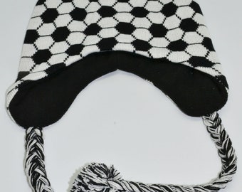 May include: Black and white knit beanie with a soccer ball pattern and a pom pom on top. The beanie has long black and white braided ties with pom poms on the ends.