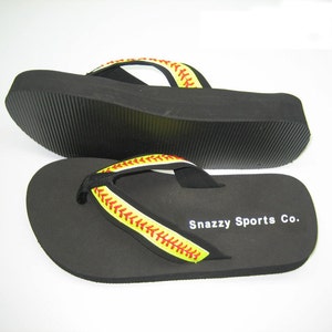 May include: Pair of black flip-flops with a yellow and red baseball stitch design on the strap. The strap says "Snazzy Sports Co."