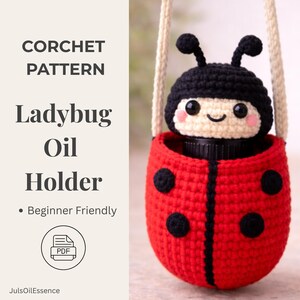 Könnte beinhalten: Ein gehäkelter Marienkäfer-Ölhalter mit schwarzem Kopf und rotem Körper mit schwarzen Punkten. Der Halter hat einen cremefarbenen Riemen und hält eine schwarze Flasche. Der Text links lautet "CORCHET PATTERN Ladybug Oil Holder" und "Beginner Friendly".