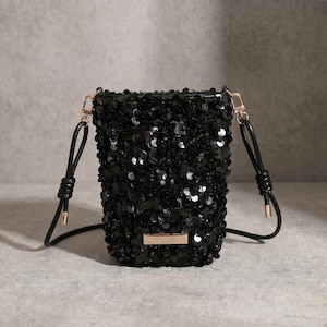 May include: Black sequin crossbody bag with a rectangular shape. The bag has a black leather strap and gold-coloured hardware. The text "CHIC CRAZY" is on a small gold-coloured plate on the front of the bag.