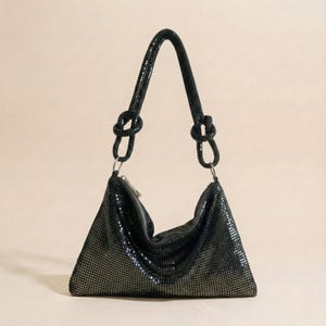 Puede incluir: Bolso de mano negro, de forma triangular, con asa de cadena anudada. El bolso está hecho de un material de malla y tiene cierre de cremallera. El asa está unida al bolso con anillos plateados. El bolso se muestra sobre un fondo neutro.