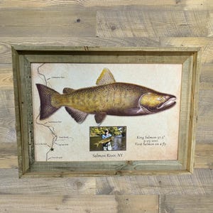 May include: Framed print featuring a detailed illustration of a King Salmon, with a map and a small photo of a person holding a fish. The text reads "King Salmon-37.5" 9-05-2021 First Salmon on a fly" and "Salmon River, NY". The frame is made of rustic wood.