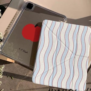 May include: Clear iPad case with a red apple design and the text "A P Apple". A striped cover with wavy blue and red lines is on top. The text "HXHStudio" is at the bottom.
