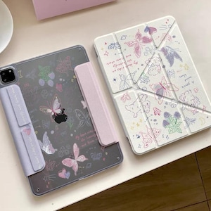 Puede incluir: Dos fundas para tabletas con diseños de mariposas. Una funda es transparente con una cubierta lavanda y gráficos de mariposas. La otra es blanca con un patrón de mariposas y flores. Ambas fundas están sobre una superficie blanca.