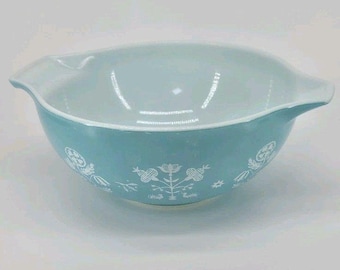 May include: A light blue mixing bowl with a white interior and two side pouring spouts. The exterior features a repeating white floral and botanical pattern encircling the bowl. The bowl has a smooth, glossy finish and a rounded base.
