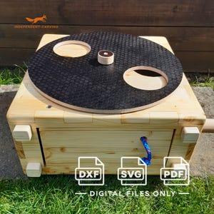 Könnte beinhalten: Eine helle Holzbox mit einer drehbaren schwarzen runden Platte, die eine Wabenstruktur und zwei kreisförmige Ausschnitte aufweist. Die Box enthält einen kleinen zentralen Knopf, eine blaue Zugschnur sowie Hinweise auf DXF, SVG und PDF-Dateien.