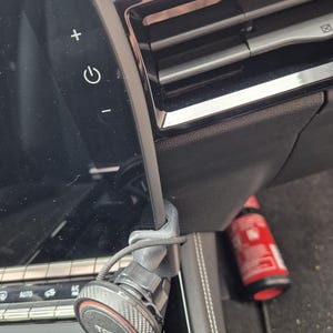 Könnte beinhalten: Schwarzes Armaturenbrett eines Autos mit einer montierten Telefonhalterung. Die Telefonhalterung ist an der Lüftungsöffnung befestigt und hat eine runde Basis mit dem Wort "TOPK" in Weiß. Ein roter Feuerlöscher ist im Hintergrund sichtbar.