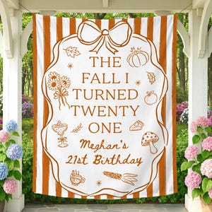 May include: A white and orange striped fabric banner featuring a large central frame with a bow at the top. The text reads THE FALL I TURNED TWENTY ONE Meghan's 21st Birthday, surrounded by illustrations of flowers, a pumpkin, an apple, a pie, a mushroom, a drink, and corn.