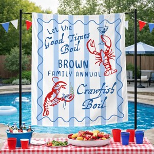 May include: A white and blue striped banner with the text "Let the Good Times Boil BROWN FAMILY ANNUAL Crawfish Boil" and illustrations of crawfish and a cocktail. The banner is displayed near a pool with a table set for a crawfish boil.