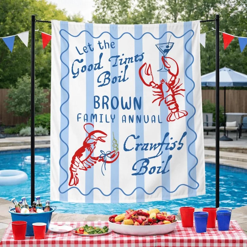May include: A white and blue striped banner with the text "Let the Good Times Boil BROWN FAMILY ANNUAL Crawfish Boil" and illustrations of crawfish and a cocktail. The banner is displayed near a pool with a table set for a crawfish boil.