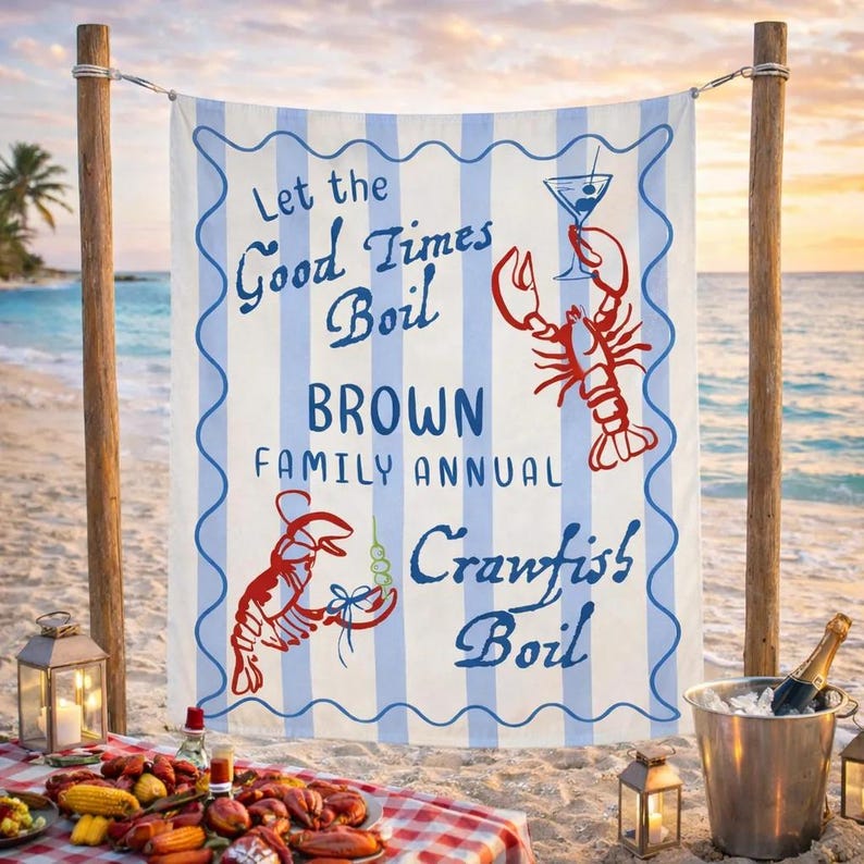 May include: A beach towel with blue and white stripes and the text "Let the Good Times Boil BROWN FAMILY ANNUAL Crawfish Boil." The towel has red lobster illustrations and is hanging on wooden poles on a beach.