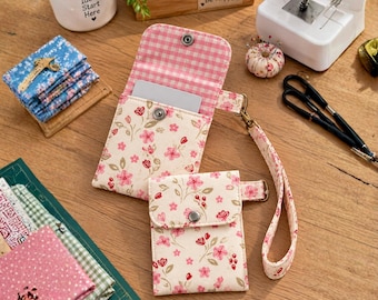 May include: A cream-colored fabric wallet and a matching smaller pouch, both featuring a pink and red floral print. The wallet has a pink gingham interior lining and a wrist strap. Both items are secured with silver-toned metal snap buttons.