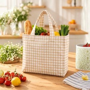 May include: A beige and white gingham patterned tote bag filled with groceries including a baguette, green lettuce, red tomatoes, a yellow lemon, and green onions. The bag features two matching fabric handles and a rectangular base.