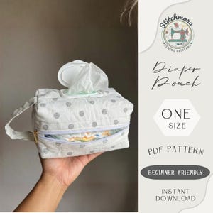 Può includere: Una pochette per pannolini bianca con un motivo a pois grigi, chiusura a cerniera e manico. La pochette ha uno scomparto per salviette e uno scomparto separato per i pannolini. Il testo "Diaper Pouch" e "ONE SIZE" sono visibili.