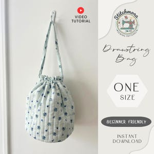 Pode incluir: Uma bolsa azul clara com cordão e padrão floral, pendurada num gancho branco. A bolsa é acolchoada e tem um fecho com cordão. A imagem também inclui texto que diz "Video Tutorial", "Drawstring Bag", "One Size", "Beginner Friendly" e "Instant Download".