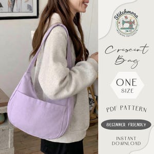 May include: A light purple crescent-shaped bag with a long shoulder strap and a front pocket. The bag is being held by a person wearing a light gray sweatshirt. The image includes text that says "Crescent Bag", "One Size", and "PDF Pattern".